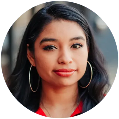 A woman with long, dark hair, wearing large hoop earrings and red lipstick, is looking directly at the camera, exuding confidence about her striking appearance.