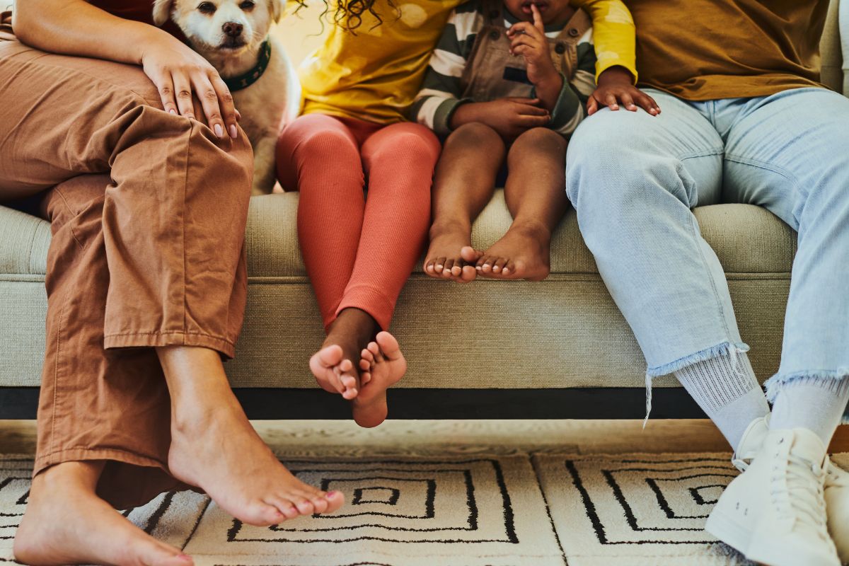 Four people and a dog sit on a couch in a living room, with close-up focus on their feet and legs. The floor features the best carpet for pets and high traffic, showcasing its durability amidst the patterned rug.