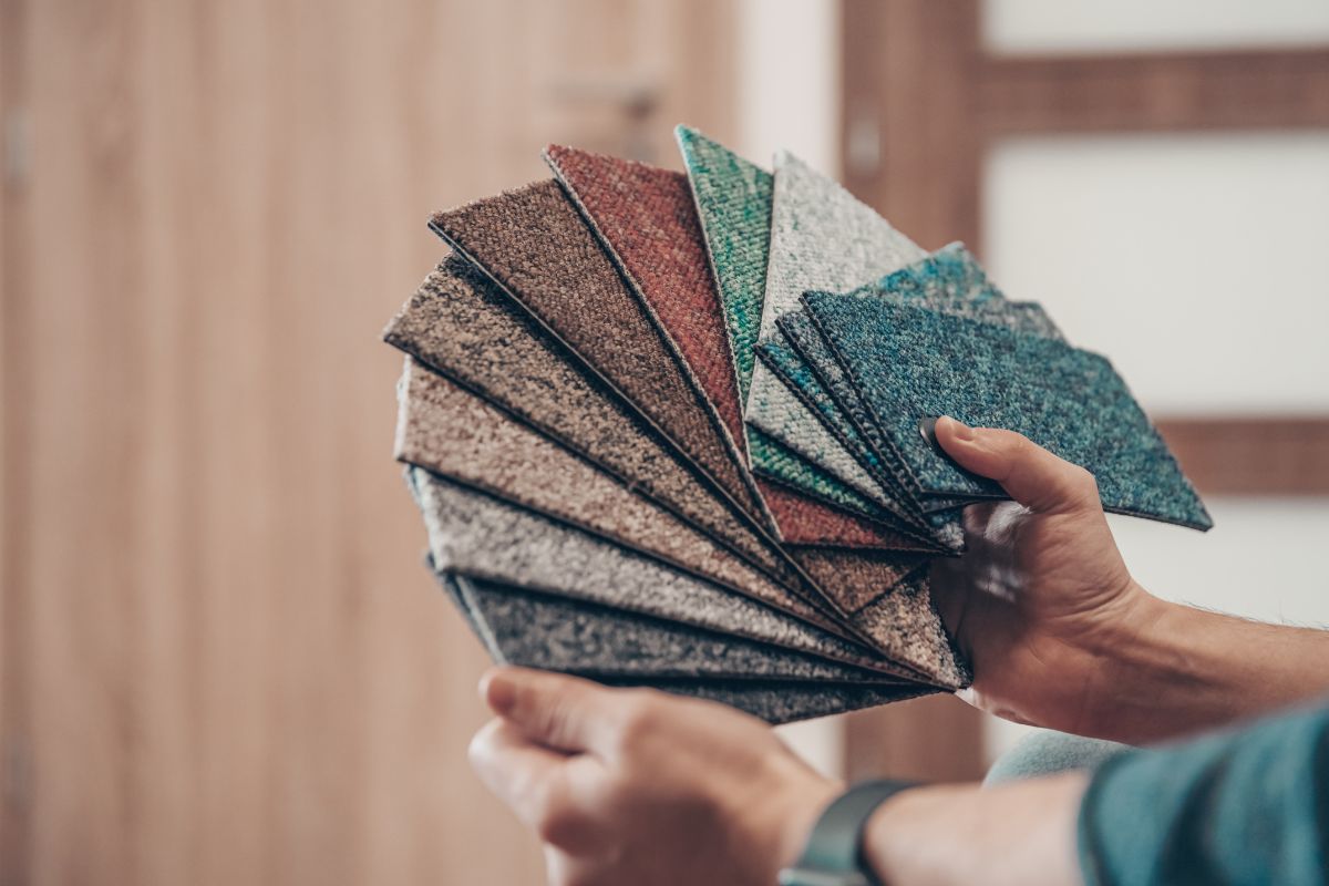 A person holding a fan of carpet samples in various colors and textures, showcasing the best carpet for pets and high traffic areas.