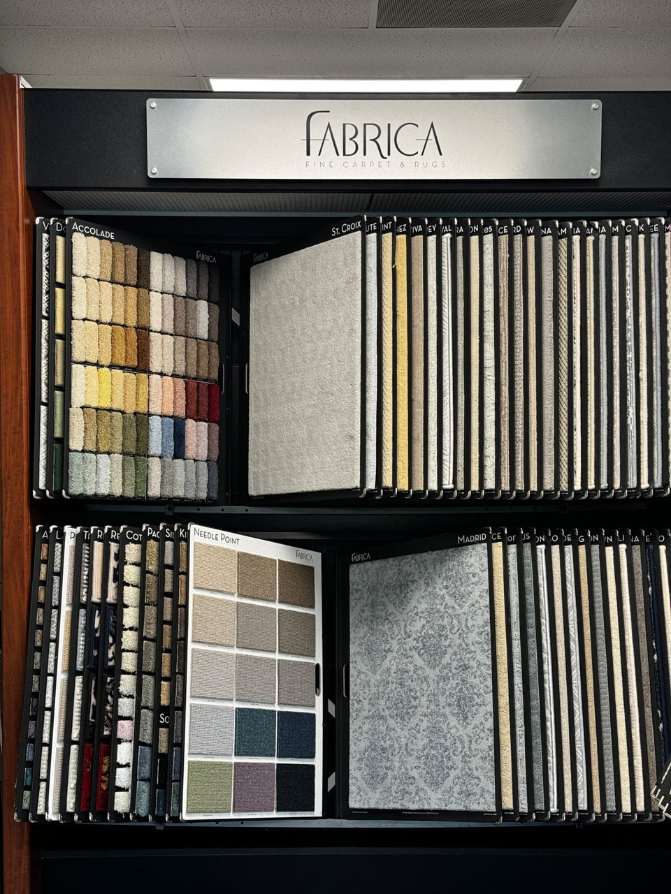 Display of various fabric swatches arranged in two rows under a sign that reads "Fabrica Fine Carpet & Rugs".