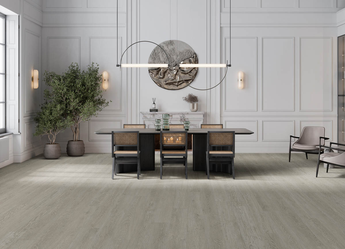 A modern dining room with a large table, four chairs, a minimalist chandelier, potted plants, and a round wall decor piece above a fireplace. The room features light wood flooring and panelled walls.