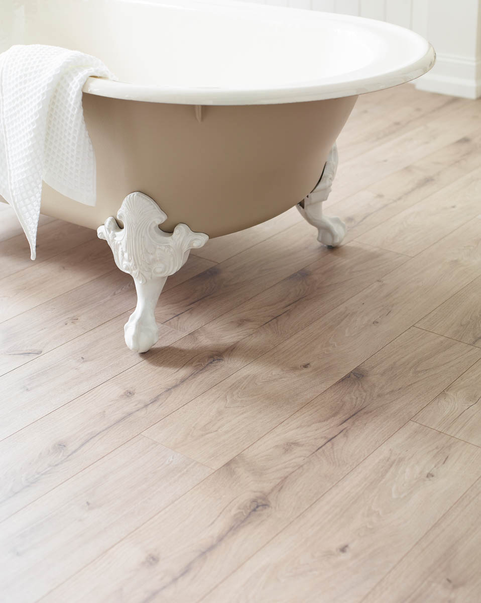 A clawfoot bathtub with a white towel draped over the edge stands on a light wood floor.