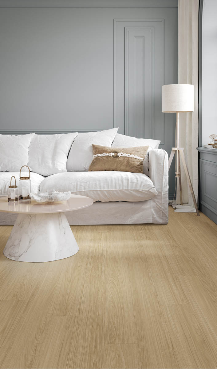 A living room with a white couch, a beige pillow, a small marble coffee table, a floor lamp, and light wood flooring.