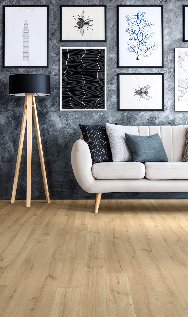 A modern living room with a light-colored curved sofa, assorted pillows, a wooden floor lamp with a black shade, and framed artwork on the textured gray wall. The floor is light wood.