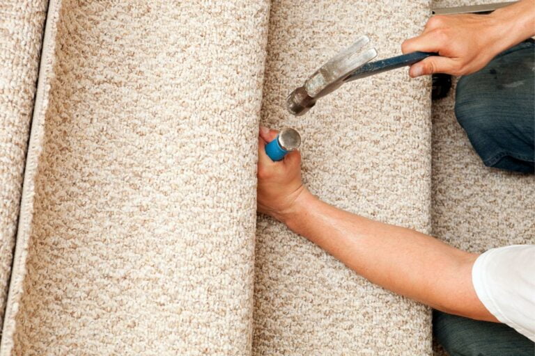 Person installing carpet using a hammer and an installation tool, ensuring the surface is perfectly smooth with precise carpet stretching techniques.