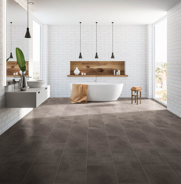 A modern bathroom with a freestanding bathtub, floating vanity, and large gray tiles installed by our expert flooring installation services. The room features white brick walls and a wooden shelf with decor items. Natural light fills the space.