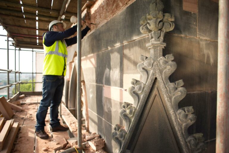 A construction worker wearing a hard hat and reflective vest engages in emergency restoration, meticulously repairing a wall on a building scaffold.