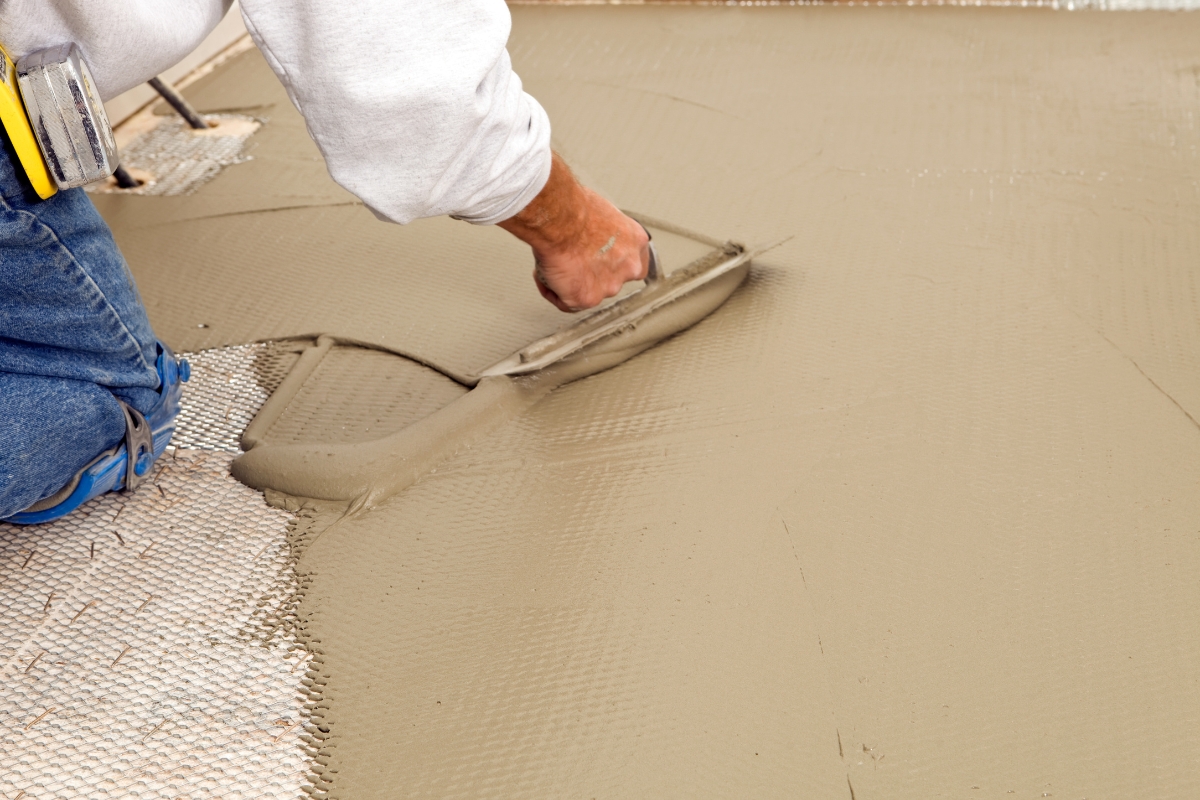 A person smooths wet concrete with a trowel on a construction site, laying the foundation for a new bathroom subfloor.