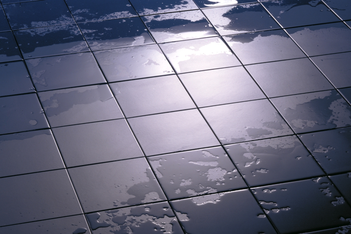 Close-up of a wet, glossy tile floor in the bathroom, with patches of water reflecting light.