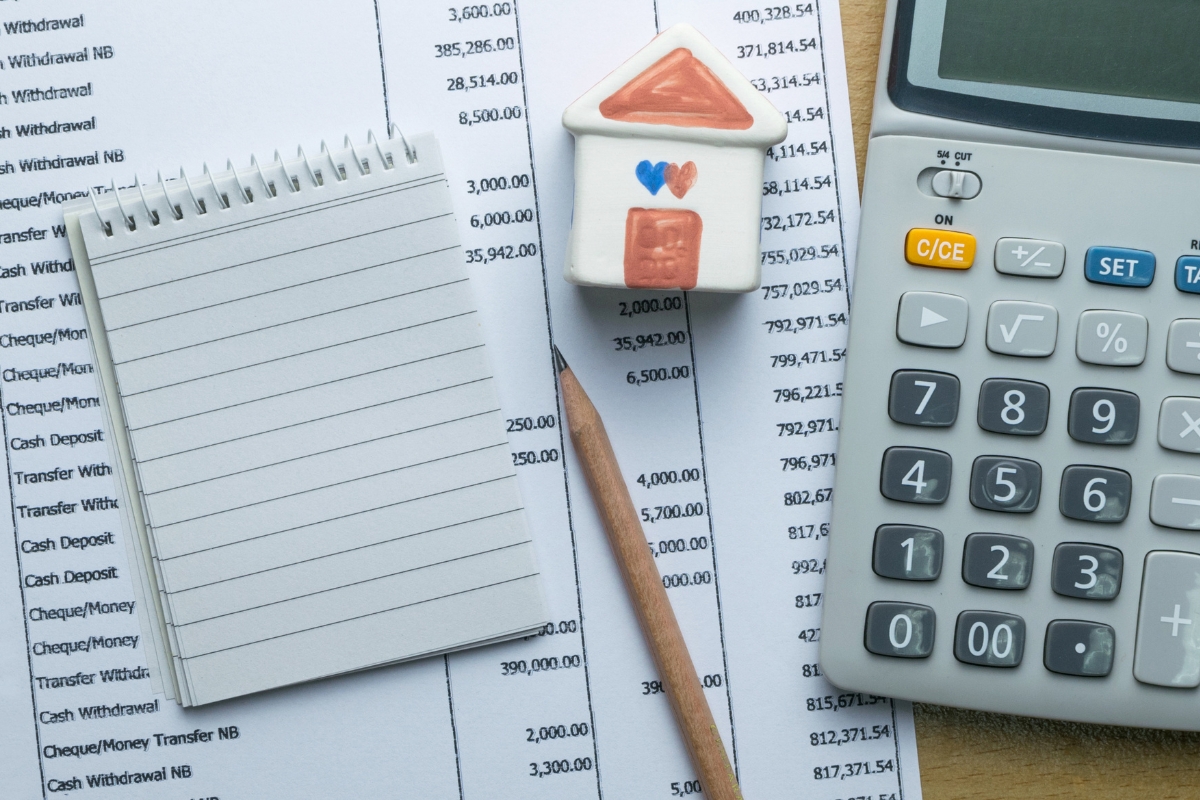 A notepad, pencil, miniature house, and calculator rest on top of bank statements, all lying neatly upon the freshly installed glue down vinyl plank flooring.