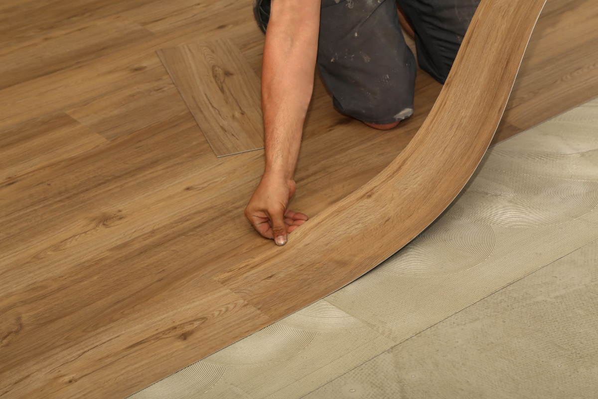 A person is installing glue down vinyl plank flooring, carefully aligning each flexible plank with the existing flooring.