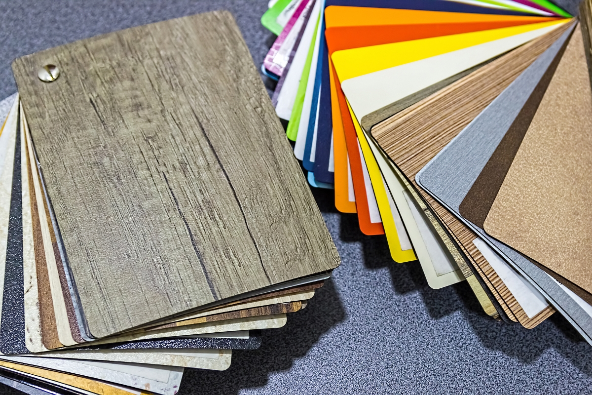 A collection of laminate samples in various textures and colors, perfect for pairing with glue down vinyl plank flooring, is fanned out on a dark surface.