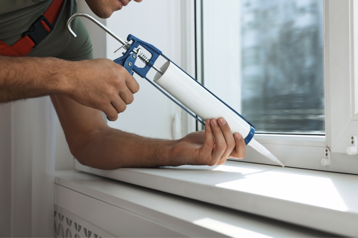 A person uses a caulking gun to apply sealant to the edge of a window frame, effectively preventing water damage.