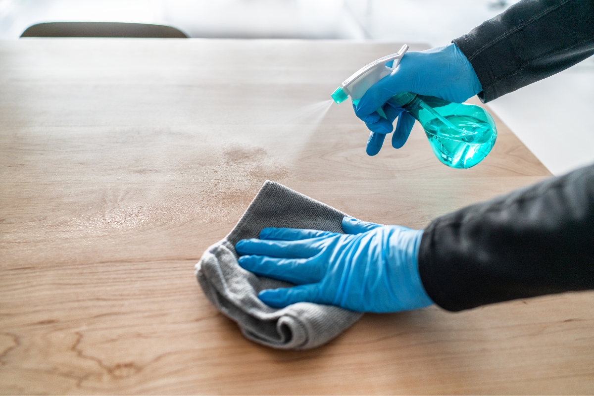 A person wearing blue gloves uses a spray bottle and cloth to clean a wooden surface, ensuring thorough water damage recovery.