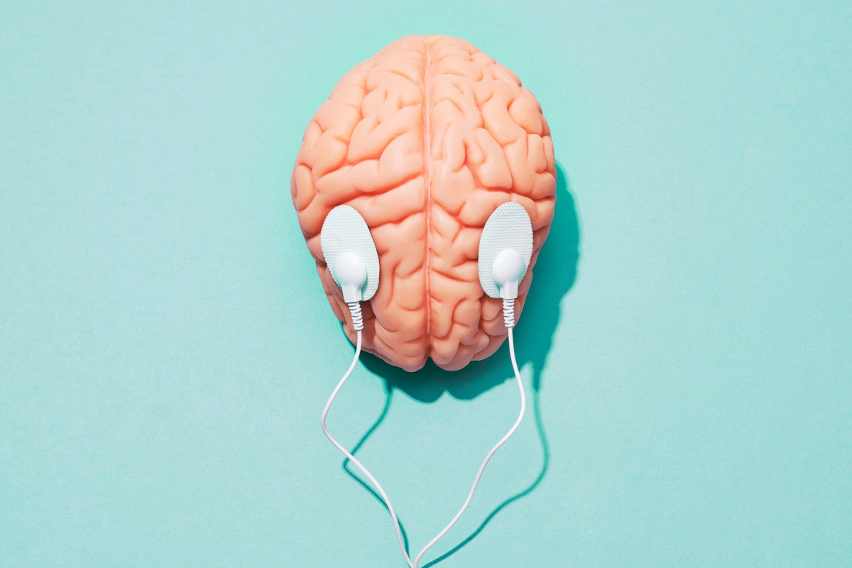 A model brain with two white wired earbuds attached, set against a teal background, serves as a stark reminder of the health risks associated with mold.