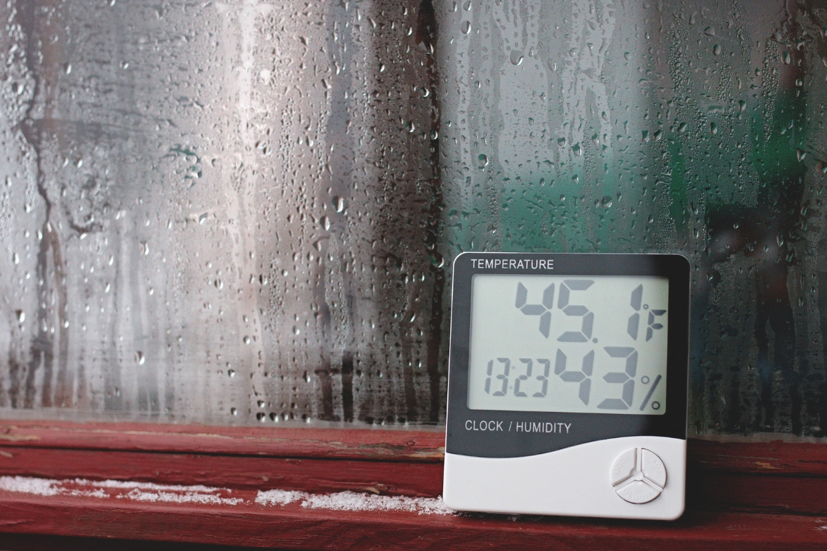 A digital temperature and humidity gauge displays 45.1°F and 32% humidity, placed on a windowsill with condensation on the glass—essential for mold removal safety.