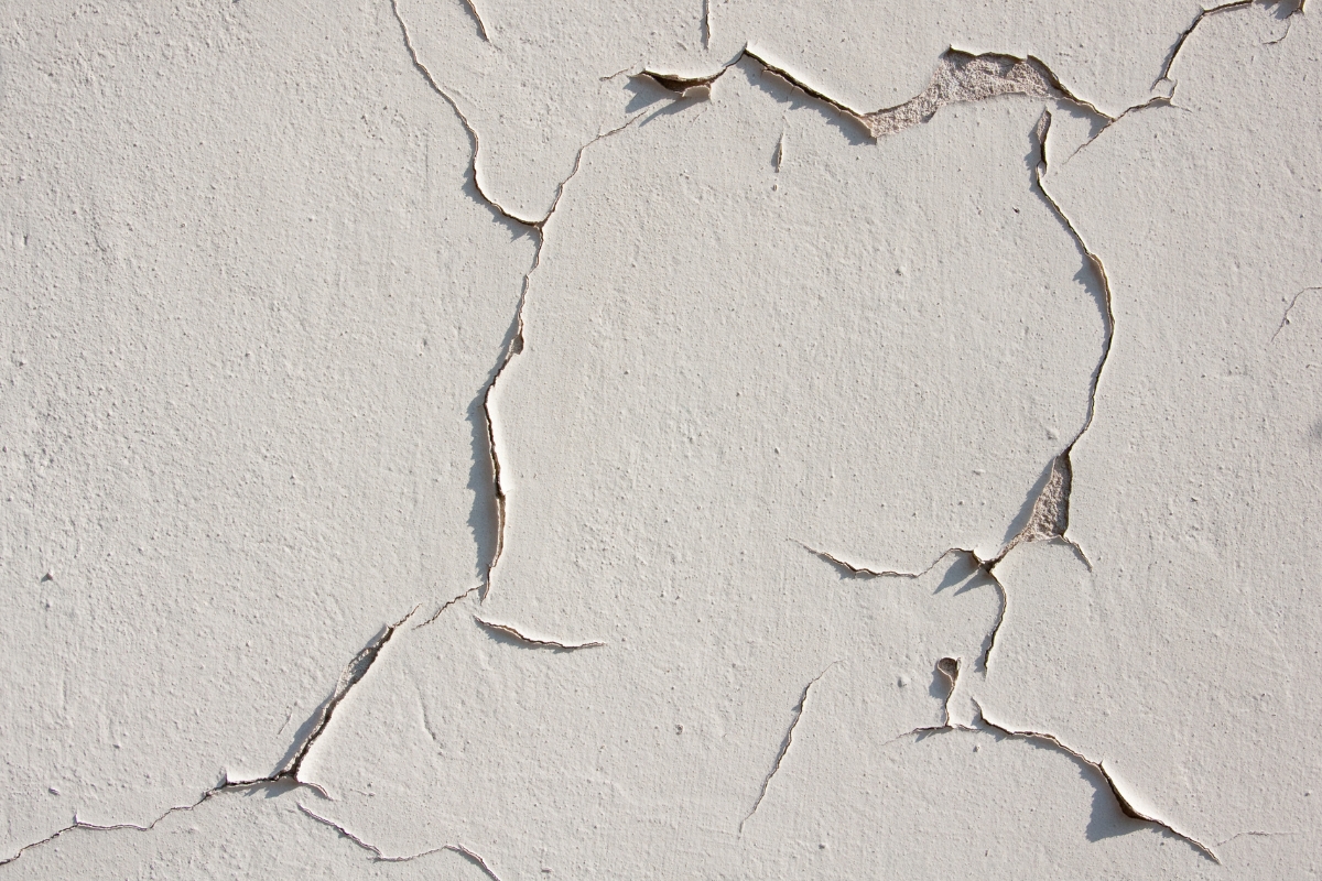 Close-up of white paint peeling off a wall, revealing the rough, cracked surface underneath—a stark reminder of the importance of proper surface preparation before painting.